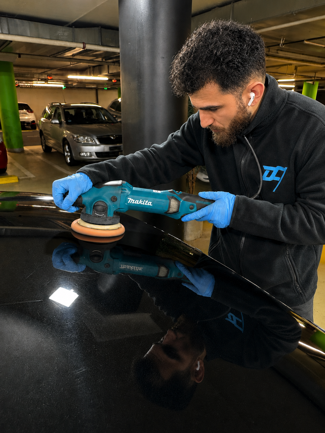 Mitarbeiter poliert schwarzen Fahrzeuglack mit einer Poliermaschine bei Drive Clean in Bern