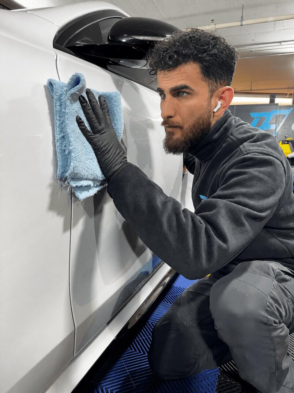 Mitarbeiter reinigt ein Fahrzeug mit einem Mikrofasertuch.